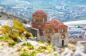 medieval holy trinity church on green flowering hill in berat