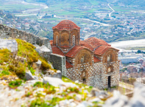 medieval holy trinity church on green flowering hill in berat